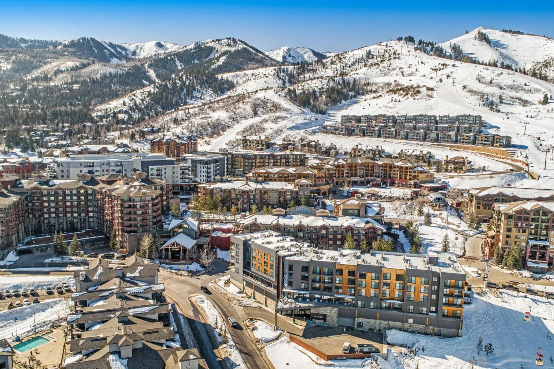 Aerial view of the Park City Mountain resort area with condominium buildings and snow-covered slopes under a clear blue sky