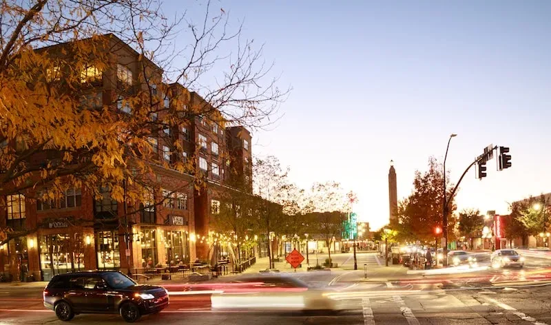 A multi-story brick building on a Sugar House street at twilight, warm lights glowing from the storefront windows and street lamps