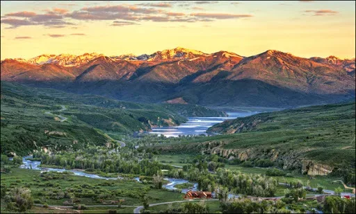 Aerial view at golden hour of the mountain valley at Victory Ranch, green foothills and a winding river running through the preserve