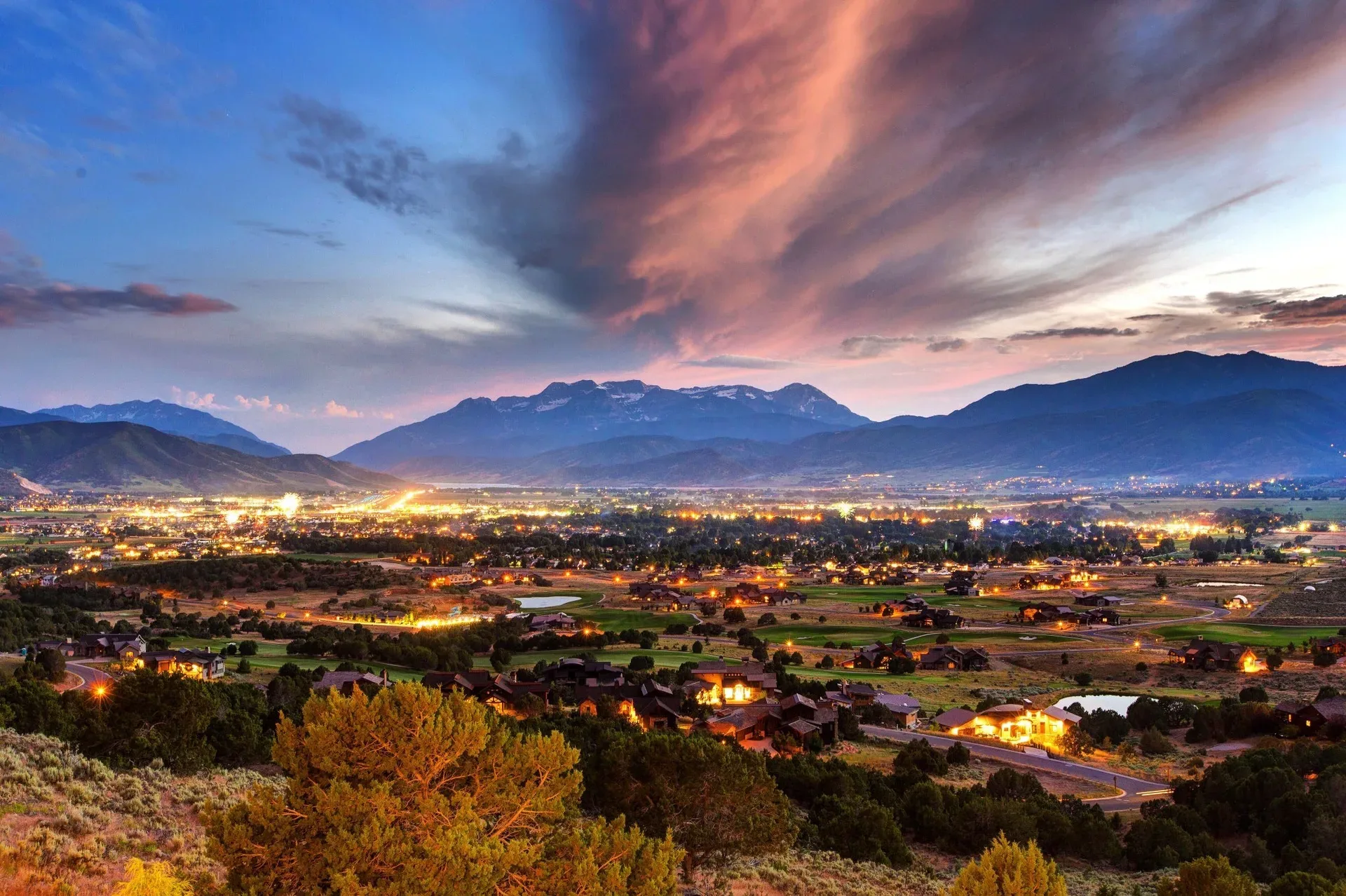 A mountain valley community at dusk with warm lights spread across the valley floor beneath the twilight peaks
