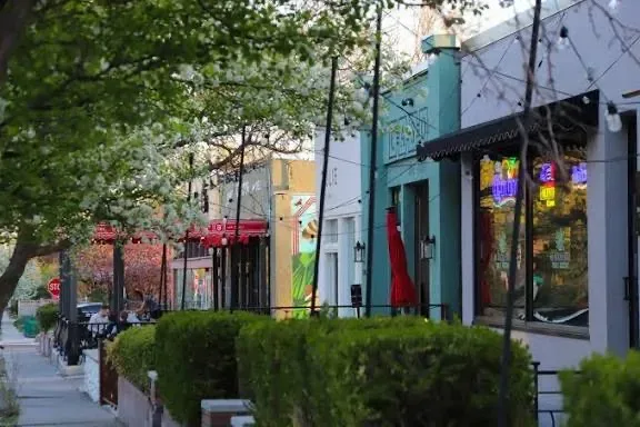 A row of small brick and stucco shopfronts with string lights at dusk on a Marmalade District corner