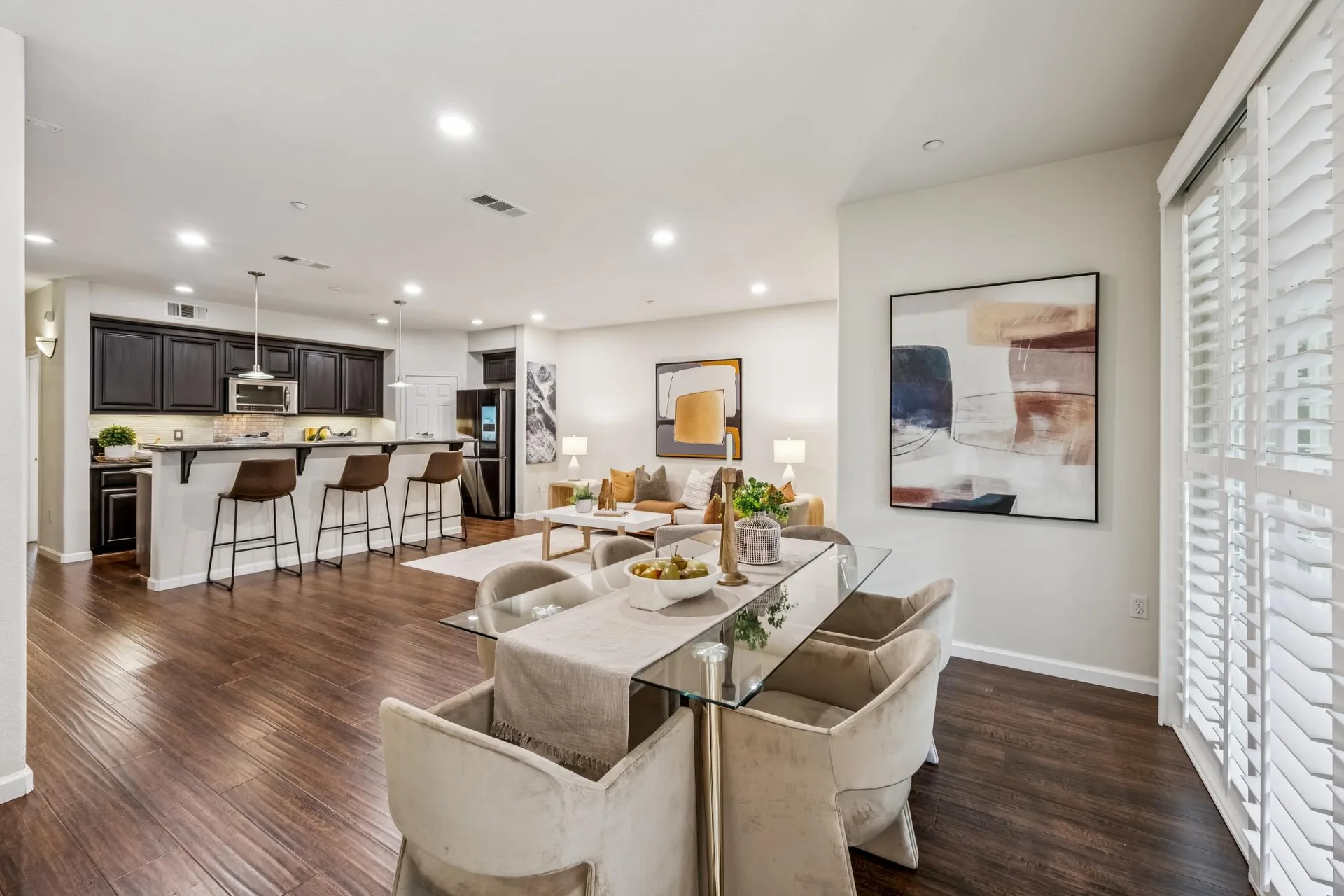 Open-concept living and dining with glass dining table and white shutters on the sliding door