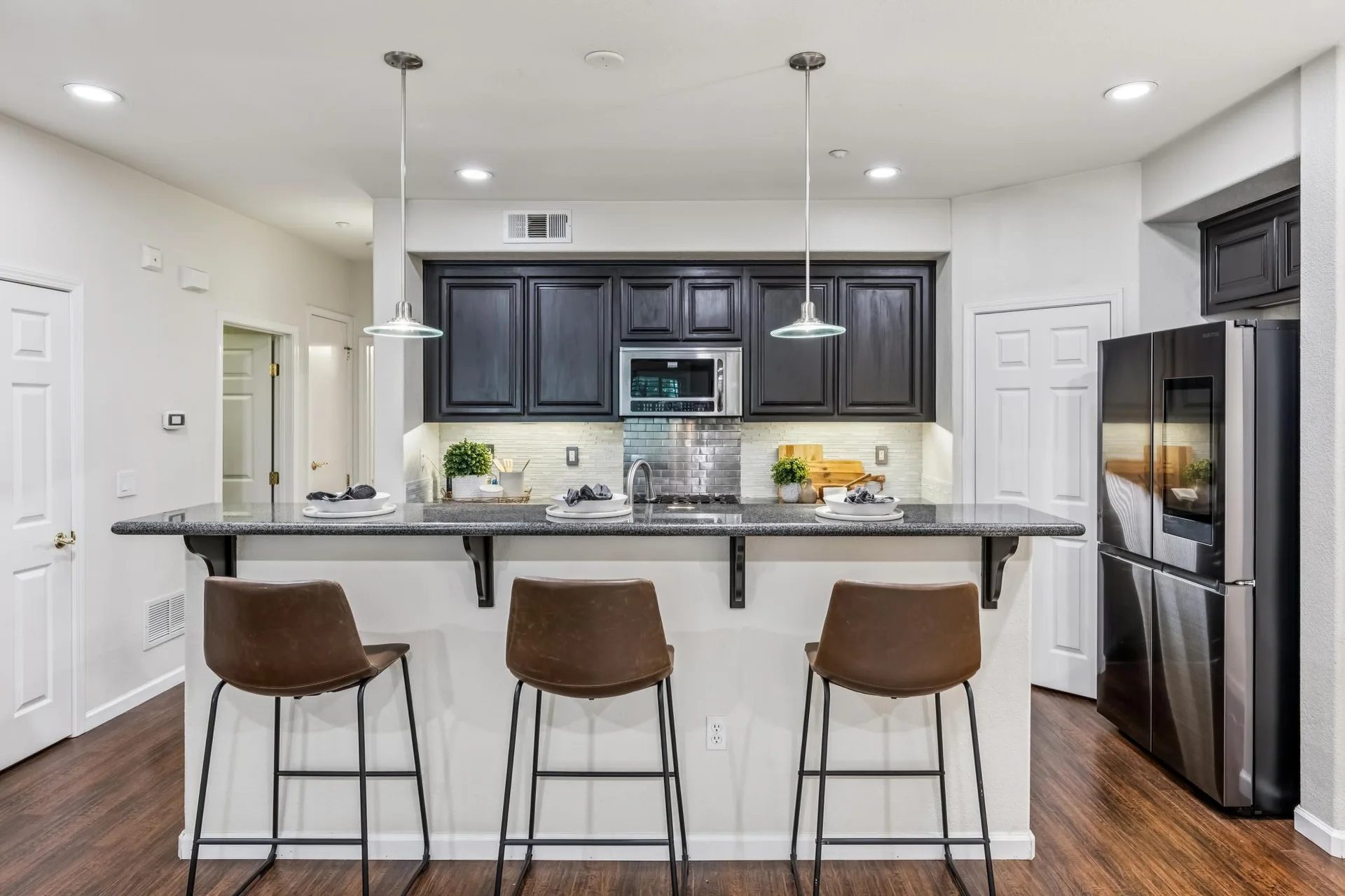 Kitchen breakfast bar with espresso cabinetry, granite counters and pendant lights