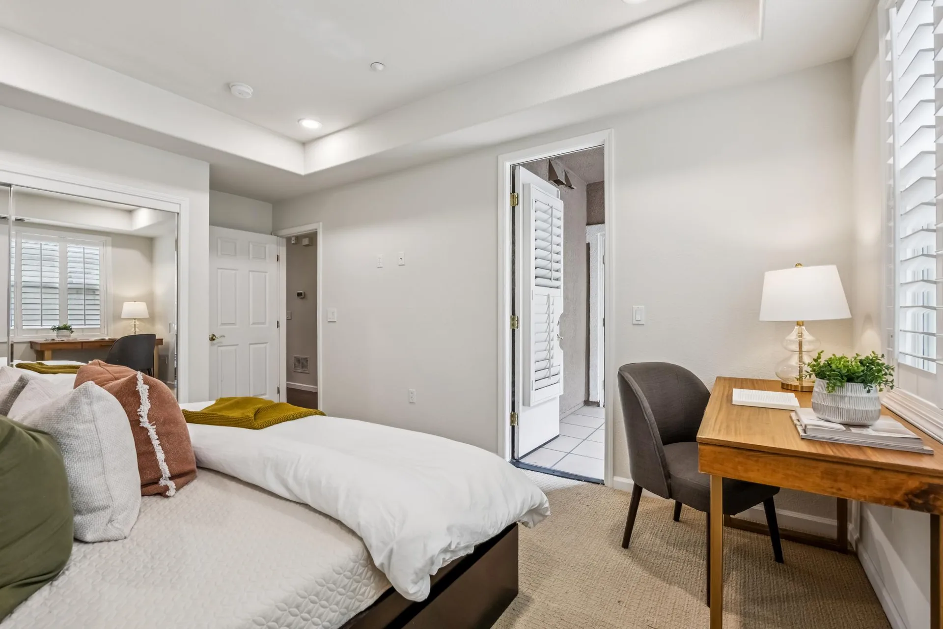 Primary bedroom with light gray walls, tray ceiling and desk corner