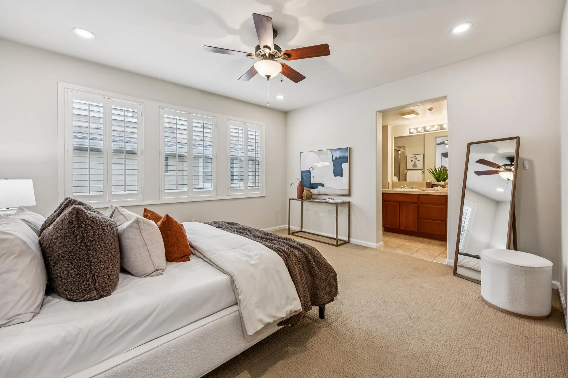 Primary bedroom with ensuite bath beyond, neutral carpet and shutters