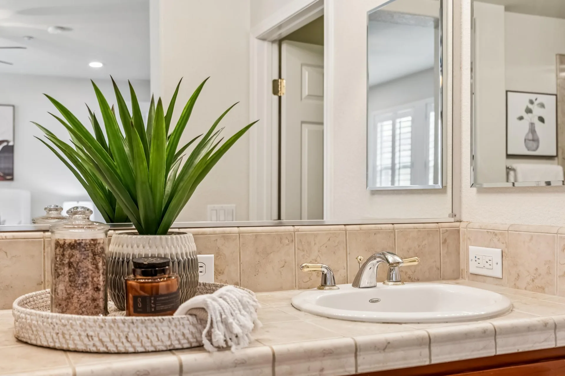 Bathroom vanity detail with tan tile countertop and wall-to-wall mirror
