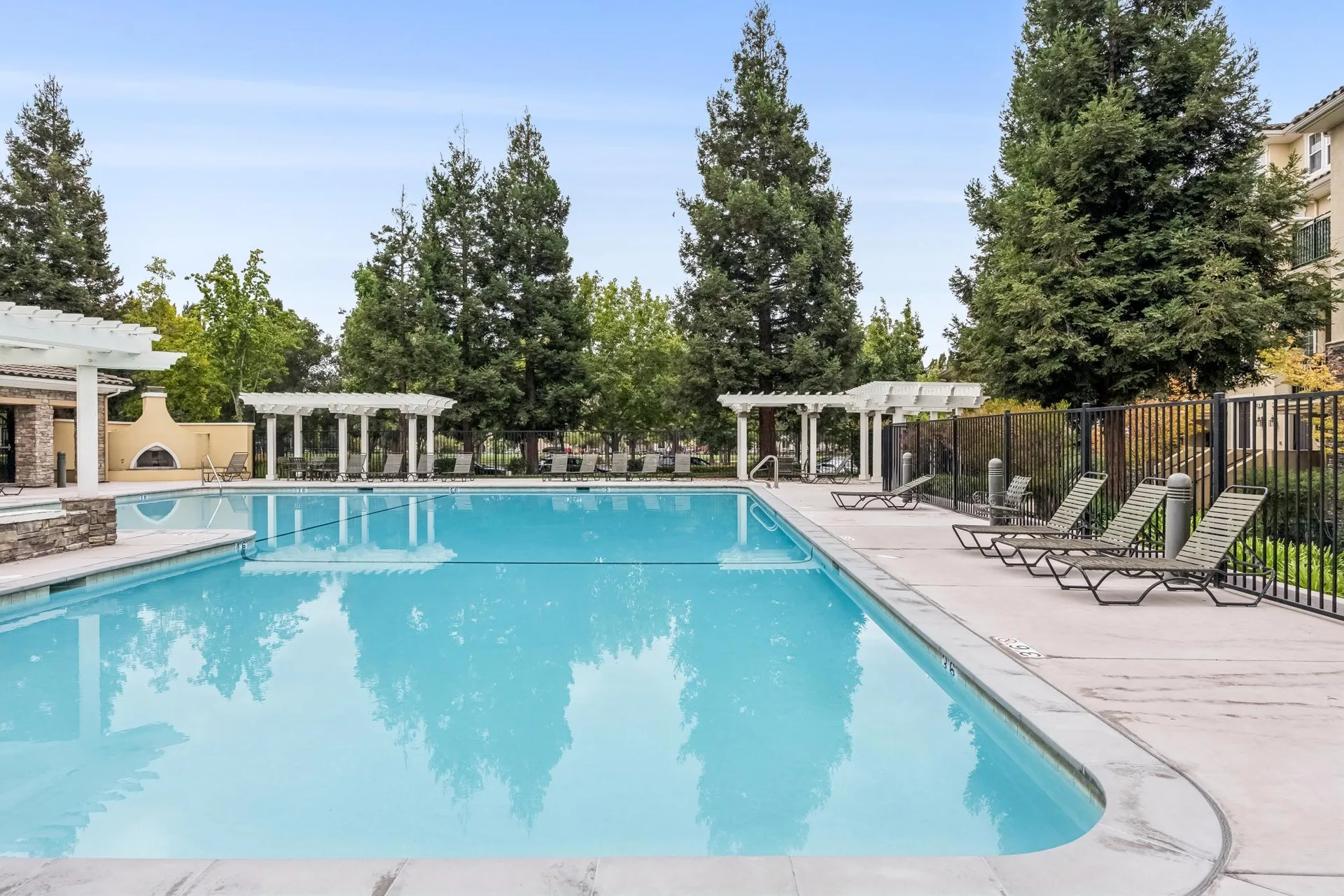Community swimming pool with white pergolas and Mediterranean landscaping