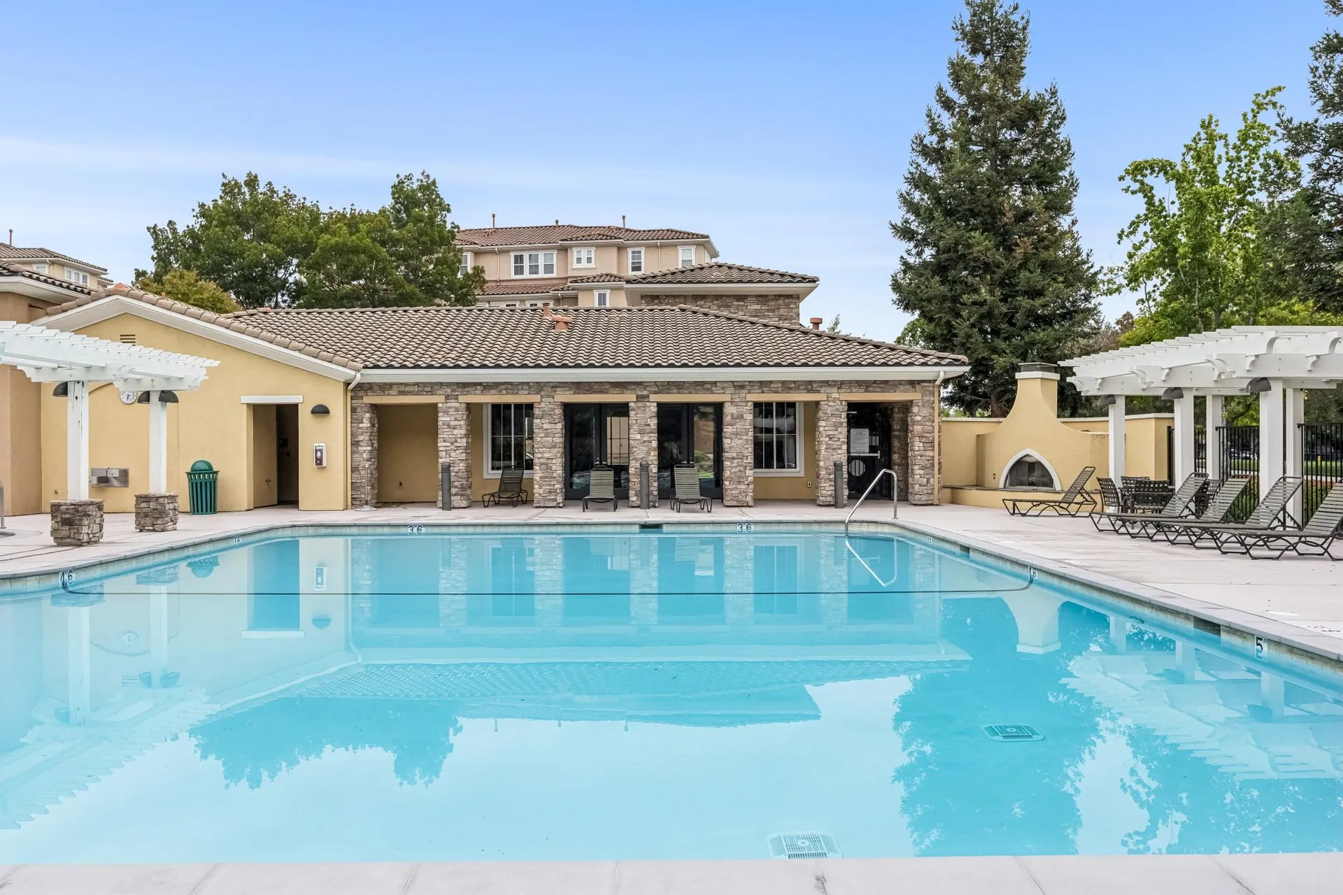 Community pool and clubhouse with stone facade, tile roof and pergolas