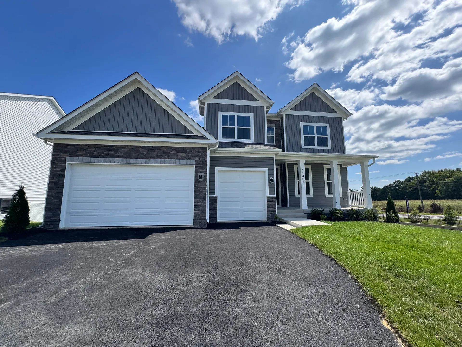 A newly built two-story home in Virginia with gray board-and-batten siding and stone accents on a bright afternoon