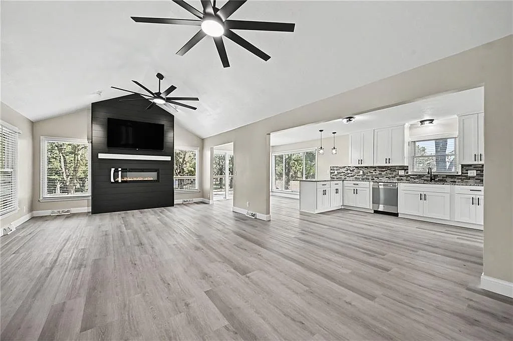 Wide view of the open-concept living room and kitchen with wood-look flooring and natural light