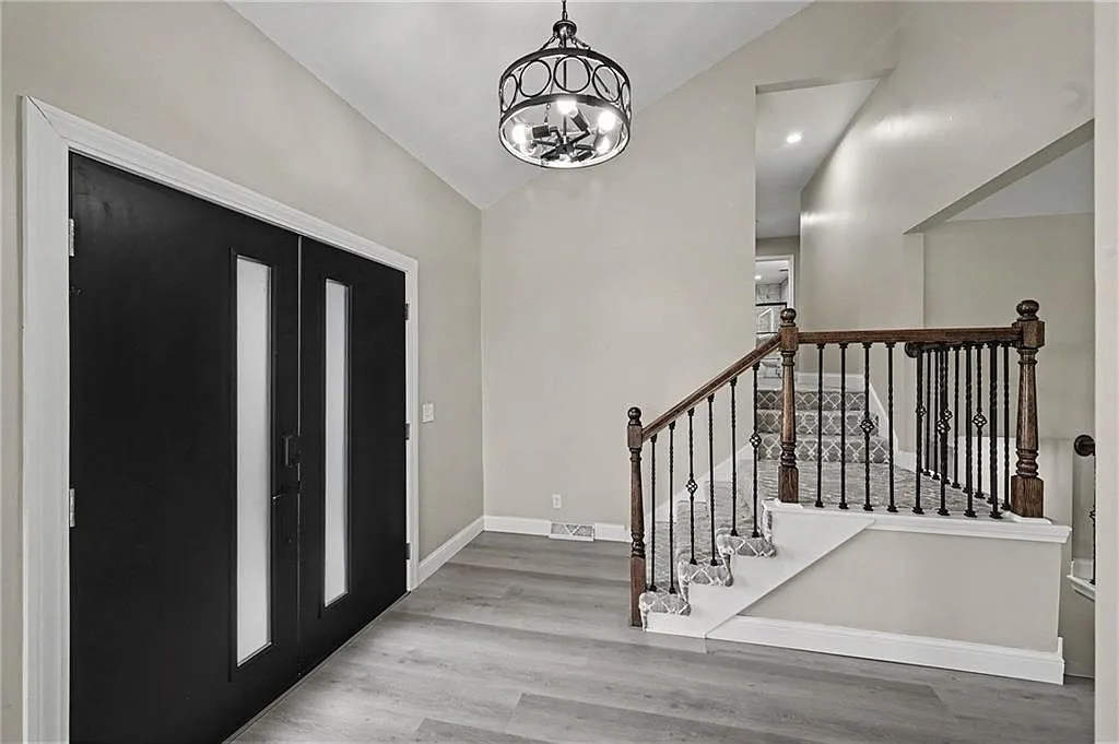 Entry foyer with matte black double doors, drum chandelier, staircase with dark handrail and patterned carpet runner