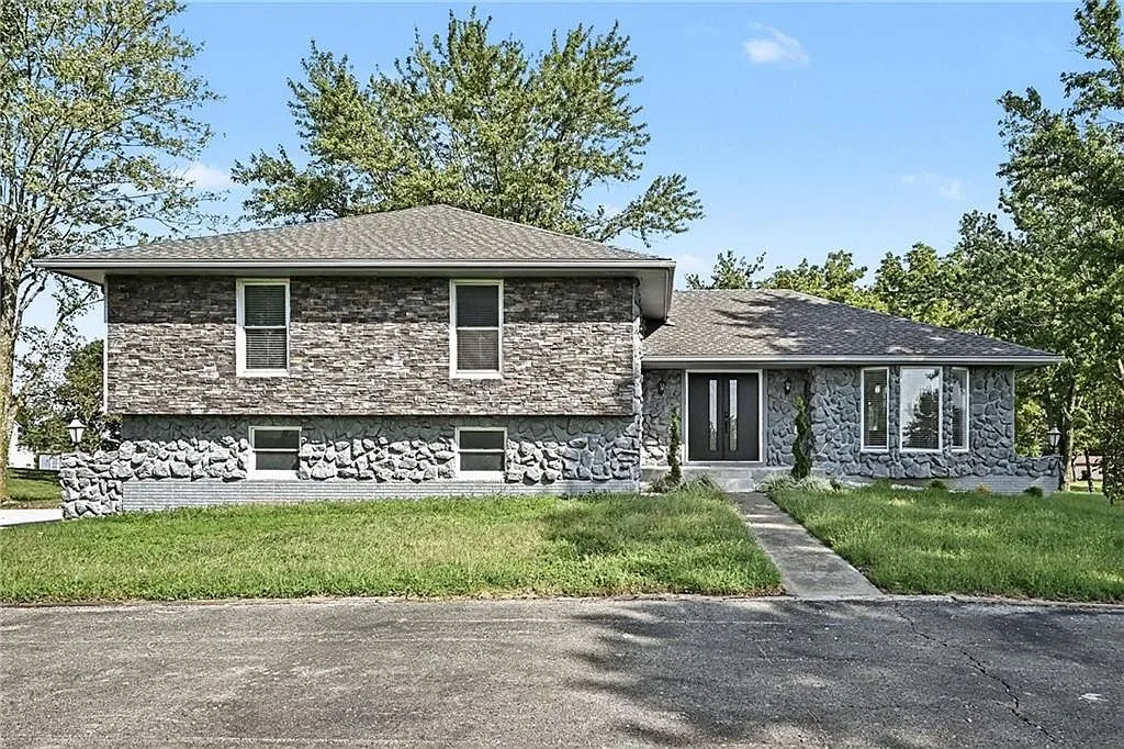 Sunlit front facade of the ranch home with stone veneer siding and a clear blue sky