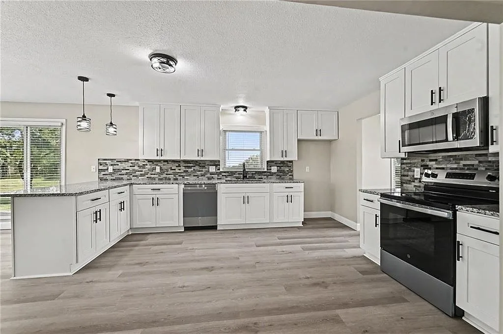 Renovated kitchen with white shaker cabinets, granite counters, tiled backsplash and peninsula