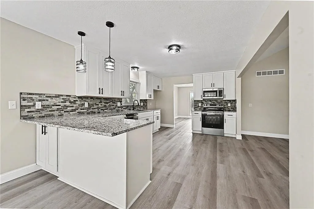 Wide angle view of the renovated kitchen with peninsula, pendant lighting and stainless steel appliances