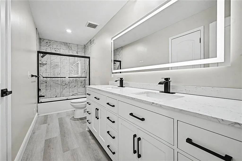 Renovated bath with white shaker vanity, marble-look counter, black hardware and tiled shower