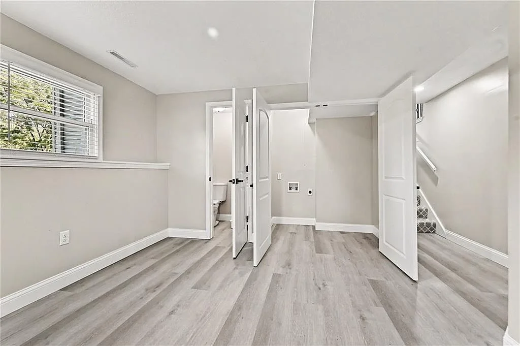 Finished basement room with vinyl plank flooring, doorway to bath and open utility entrance