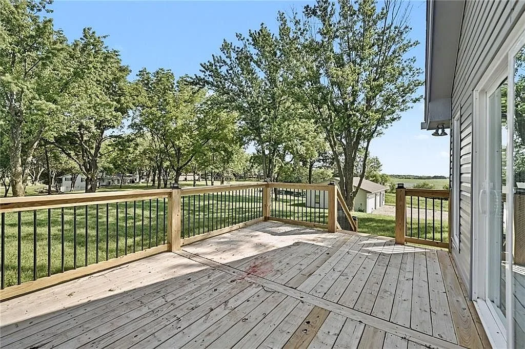 Wood deck with black metal balusters overlooking the property grounds and distant tree line