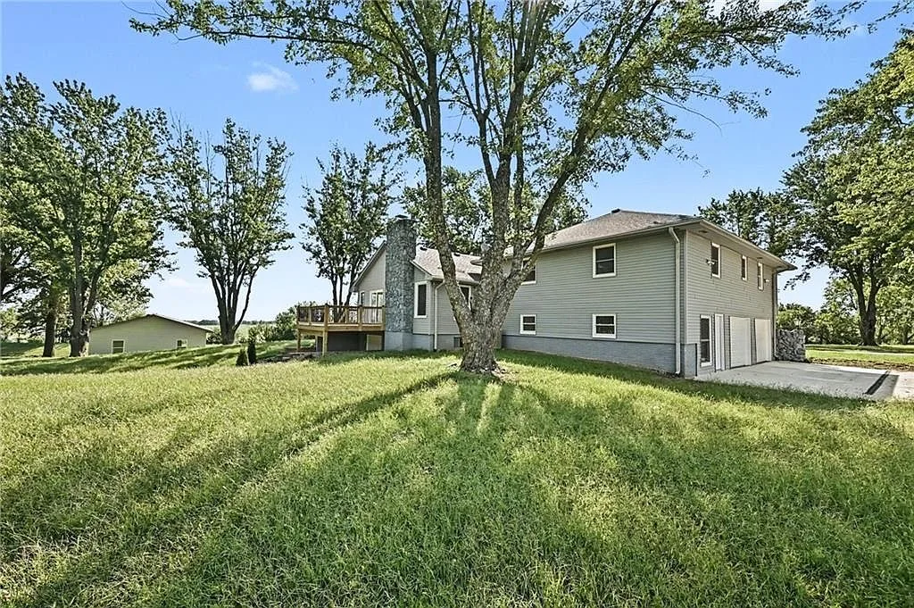Rear view of the ranch house on a large grassy lot with raised wooden deck and side entry garage