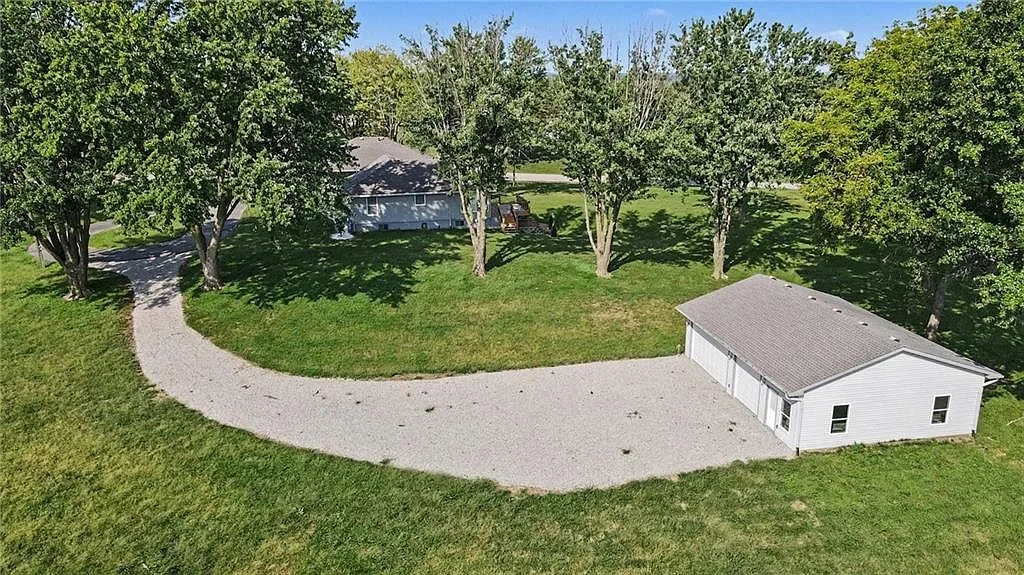 Aerial view of the property grounds, gravel drive, ranch home and timber around the lot