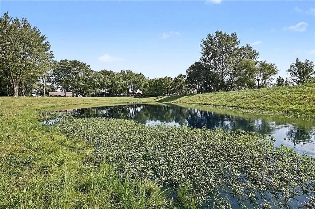 Private pond on the property with grassy banks and mature trees in the background