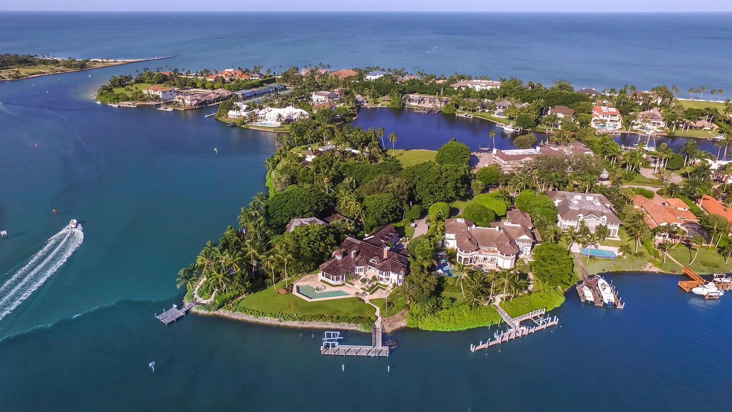 Aerial view of a Naples coastal peninsula with luxury estates, private docks, and a boat heading out on open water