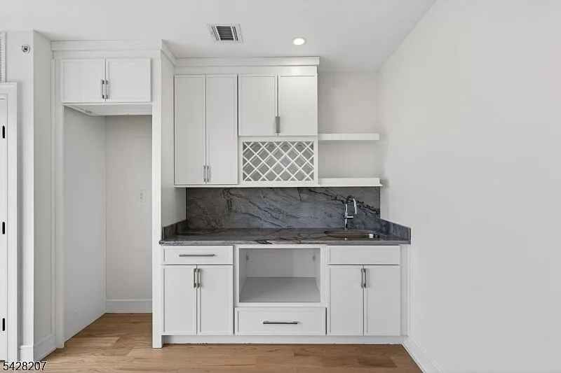 Wet bar kitchenette with white cabinetry and dark stone counters