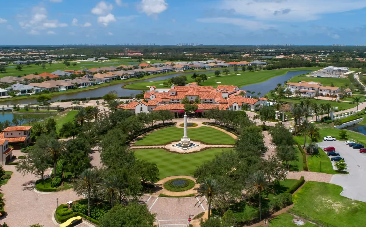 Aerial view of a Mediterranean-style clubhouse and surrounding golf course in a Naples country club community