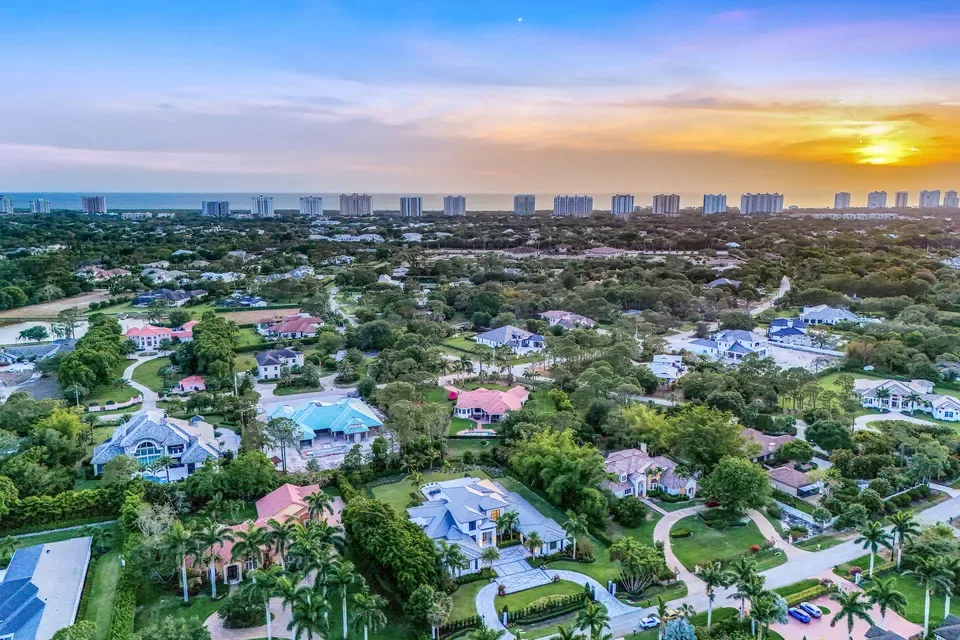 Aerial view of a Naples residential neighborhood at sunset, with coastal homes, palm trees, and the Gulf horizon