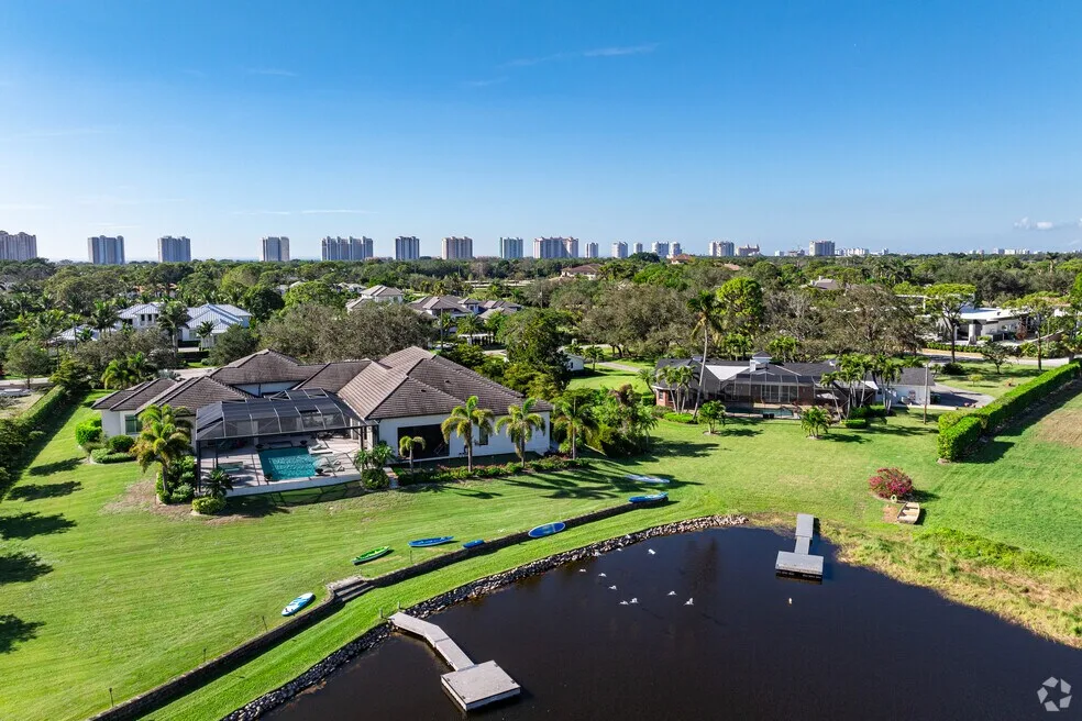 Aerial view of a lakefront Naples estate with a pool, manicured lawn, and private dock in sunny daylight