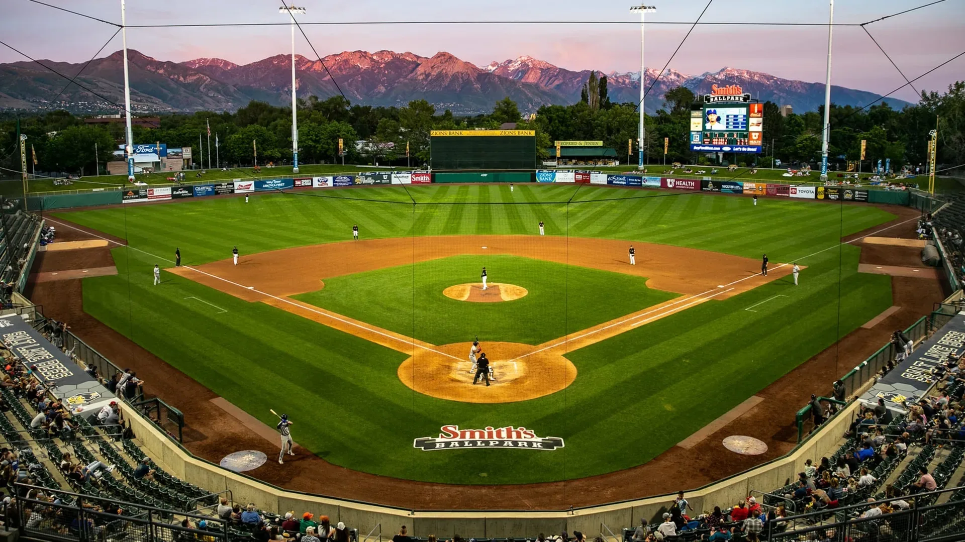 A Salt Lake Bees game at Smith's Ballpark at sunset, with the mountain range rising behind the outfield