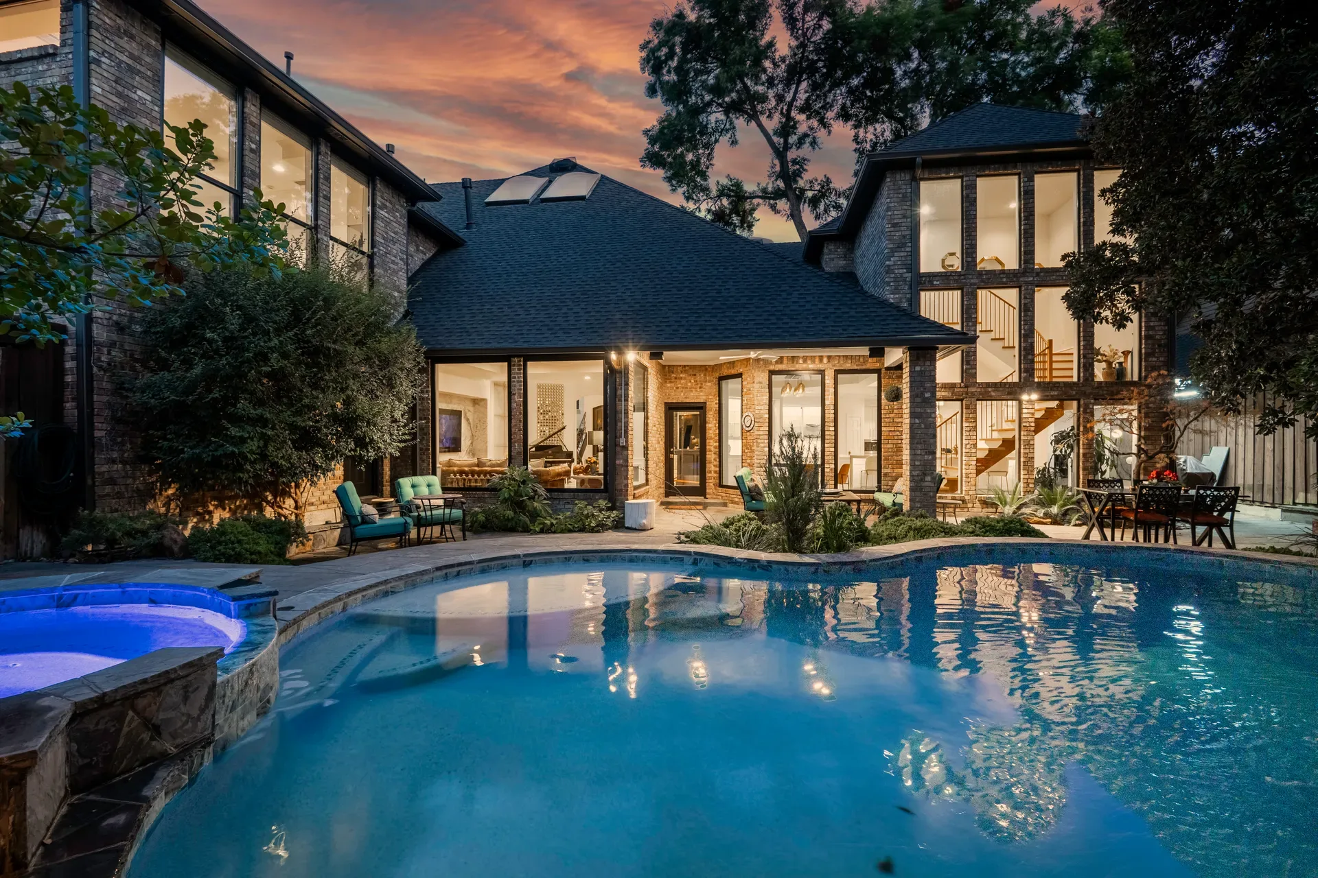 Real photo of a backyard pool and spa in the evening, glowing blue water at dusk