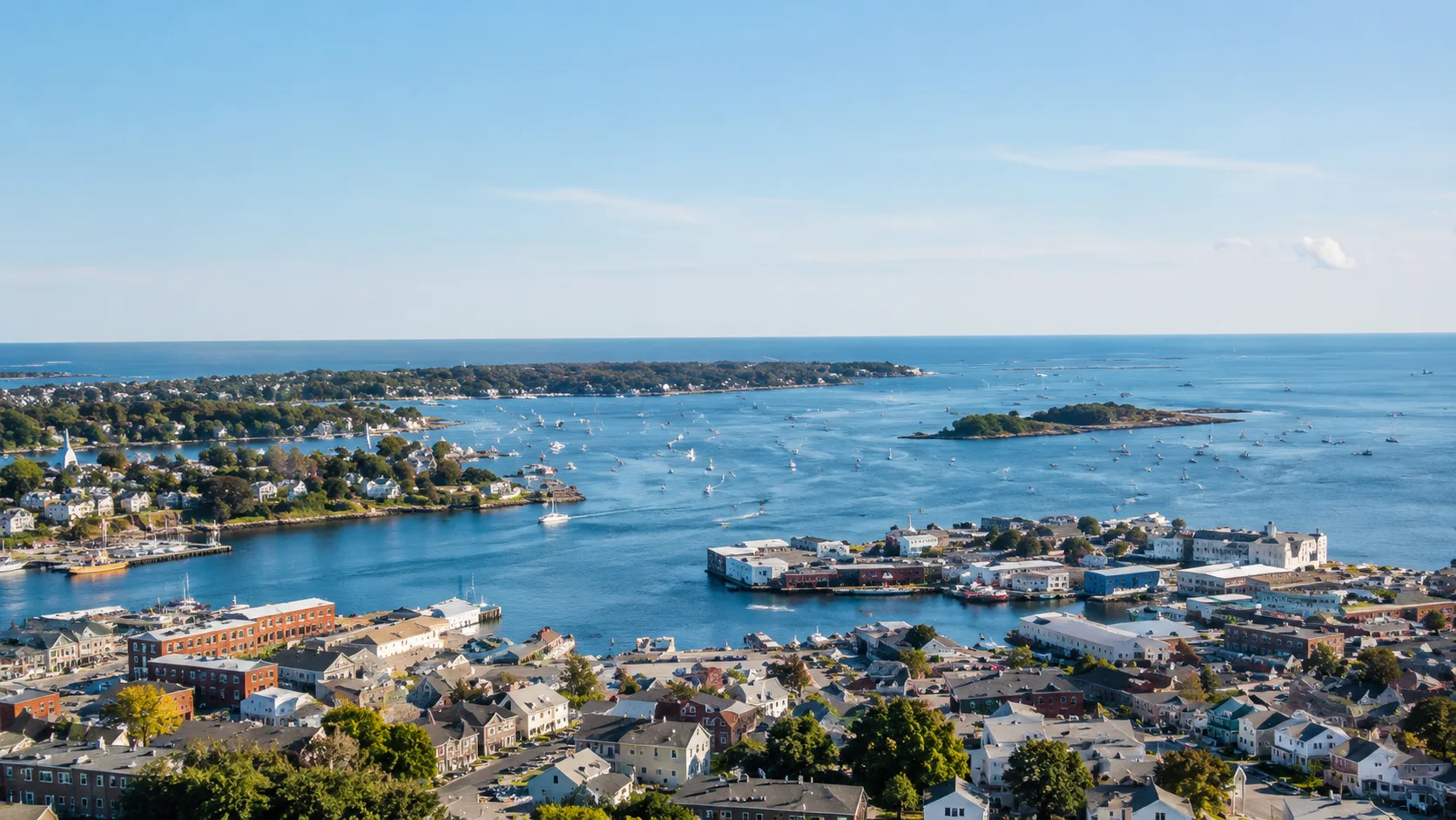 Aerial view of a coastal North Shore harbor town with boats on the water beneath a clear blue sky