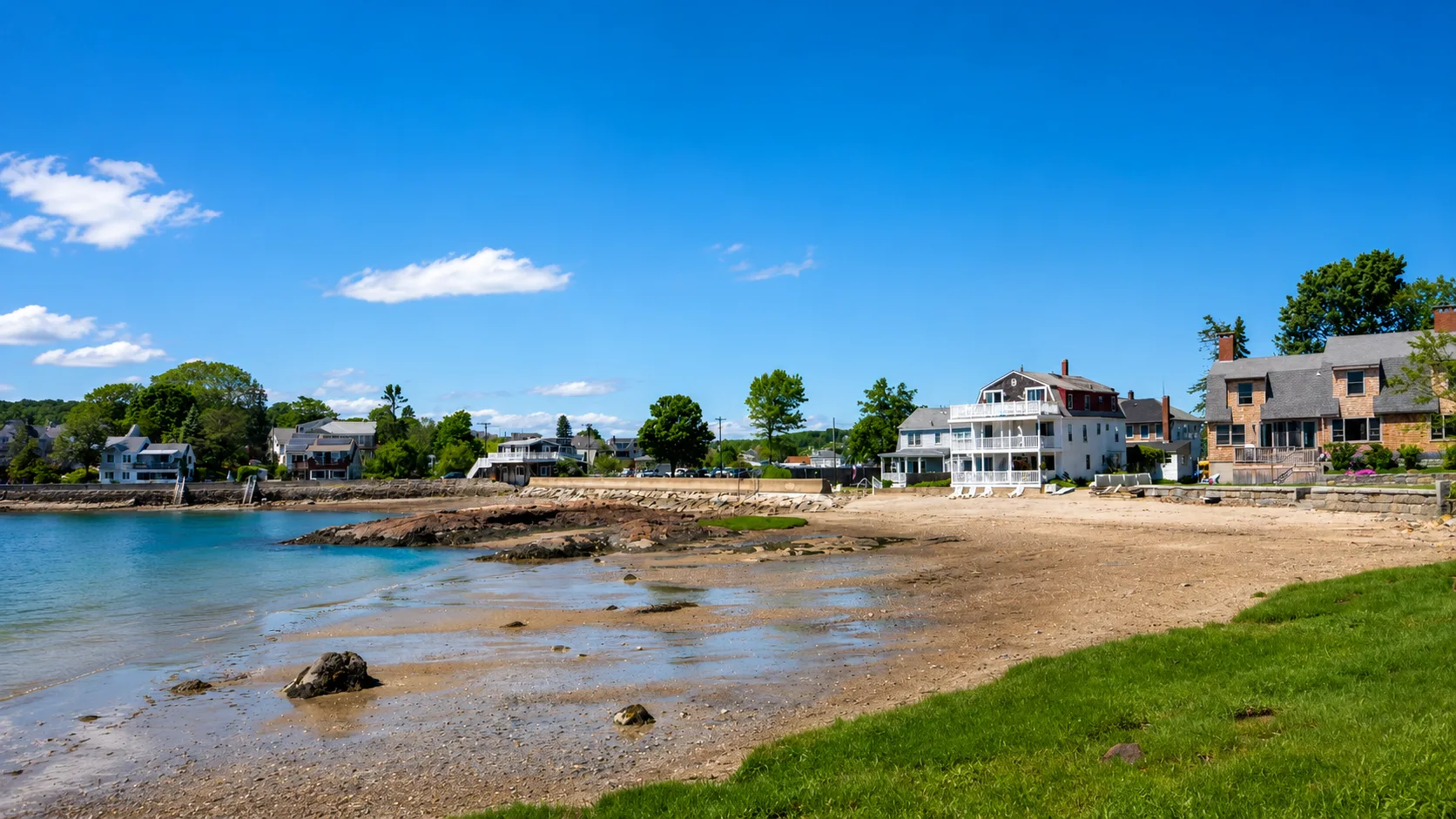 Shingle-style homes along a sandy North Shore beach under a clear blue sky