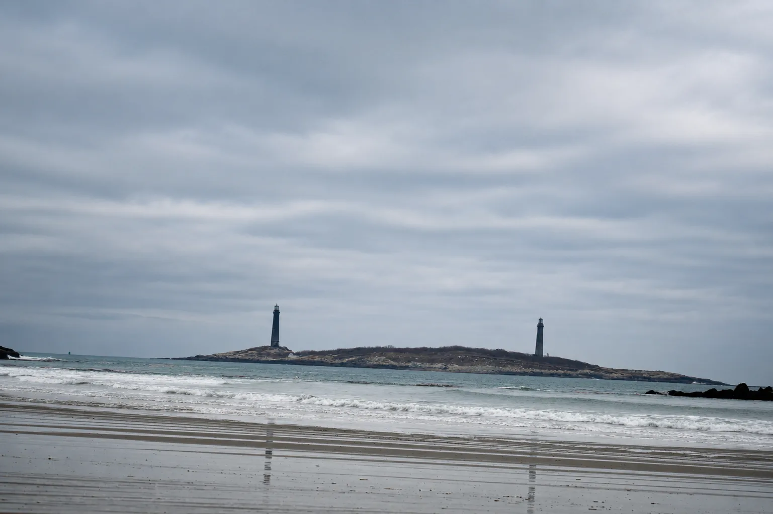 Two lighthouses on a rocky island off the North Shore coast, seen from the beach