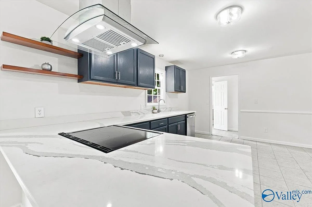 Designer kitchen with quartz countertops, dark cabinetry, floating shelves, and a stainless range hood