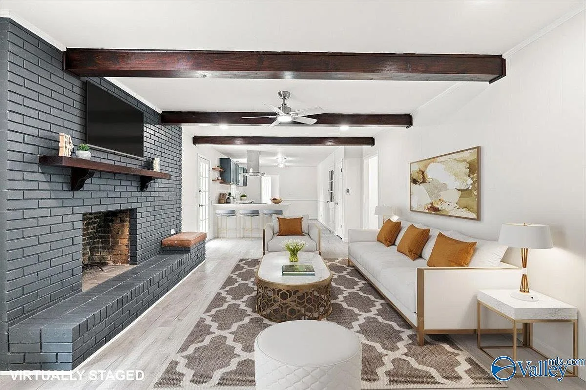 Living room with a brick fireplace, wood ceiling beams, and a view into the kitchen