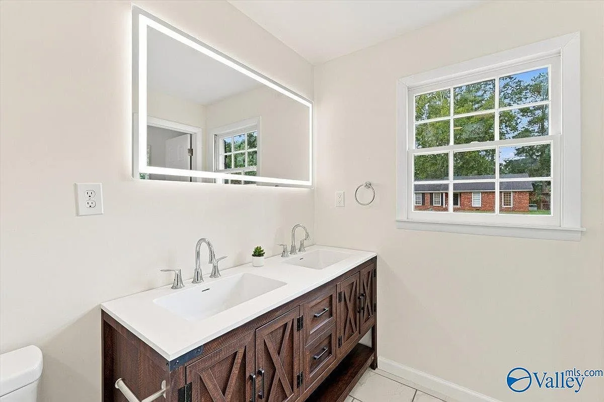 Primary bath vanity with dual sinks, wood cabinets, and an LED mirror