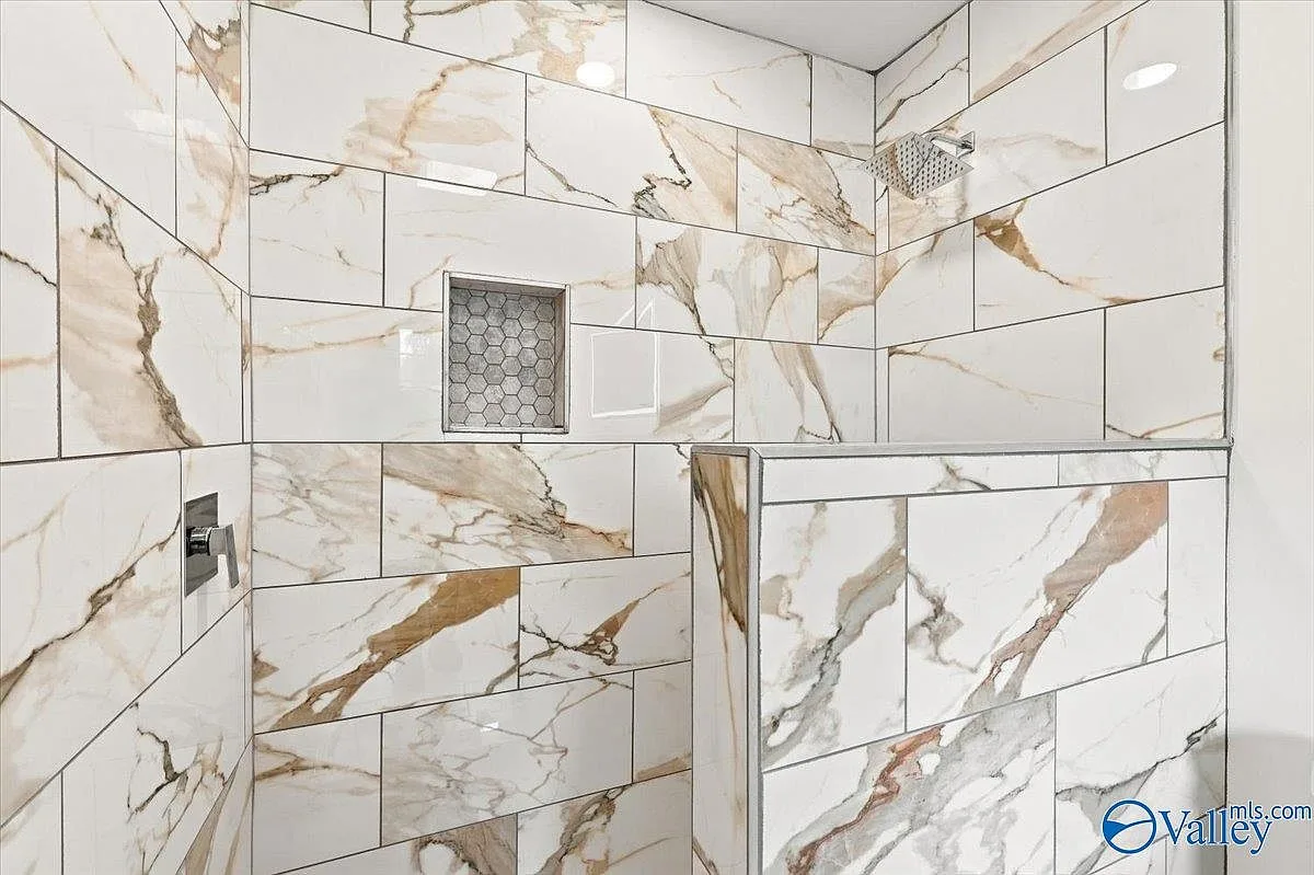 Large walk-in shower with marble-look porcelain tile, gold veining, and an inset tile niche