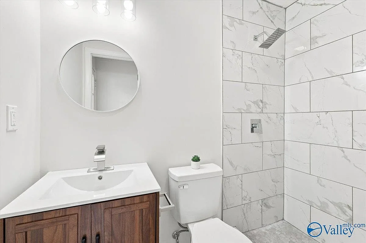 Bathroom with a dark wood vanity, circular mirror, and subway-style tile shower