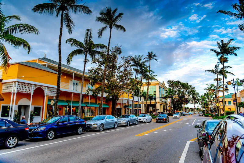 Bright tropical commercial boulevard with yellow stucco storefronts and tall palm trees in Olde Naples