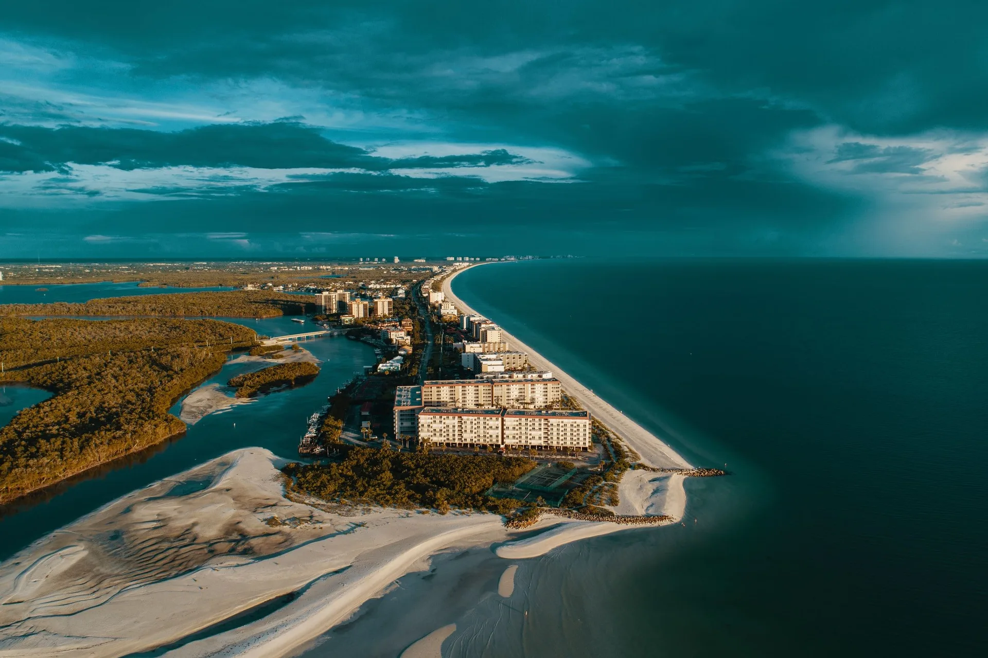 Aerial view of the Naples coastline where Gulf-front buildings sit between a protected inlet and a white sand beach