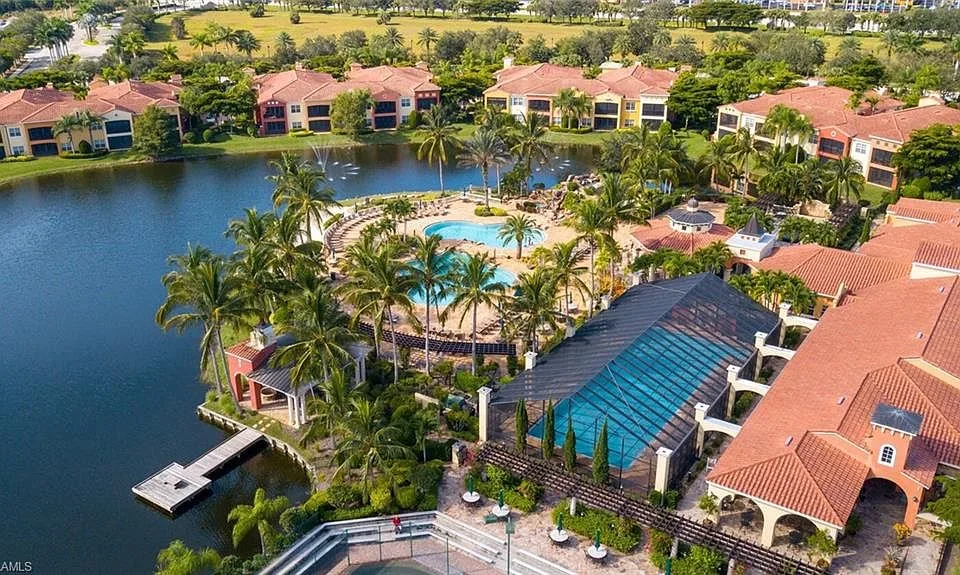 Aerial view of a Naples community amenity center with a pool, loungers, and a lake in a Mediterranean-style neighborhood