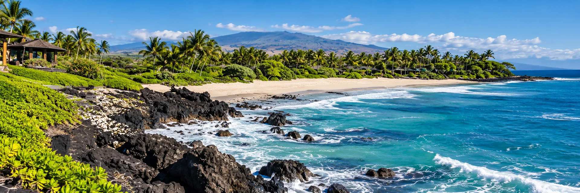 Sandy Kūkiʻo Beach with jagged lava rock in the foreground and turquoise ocean, bordered by palms.