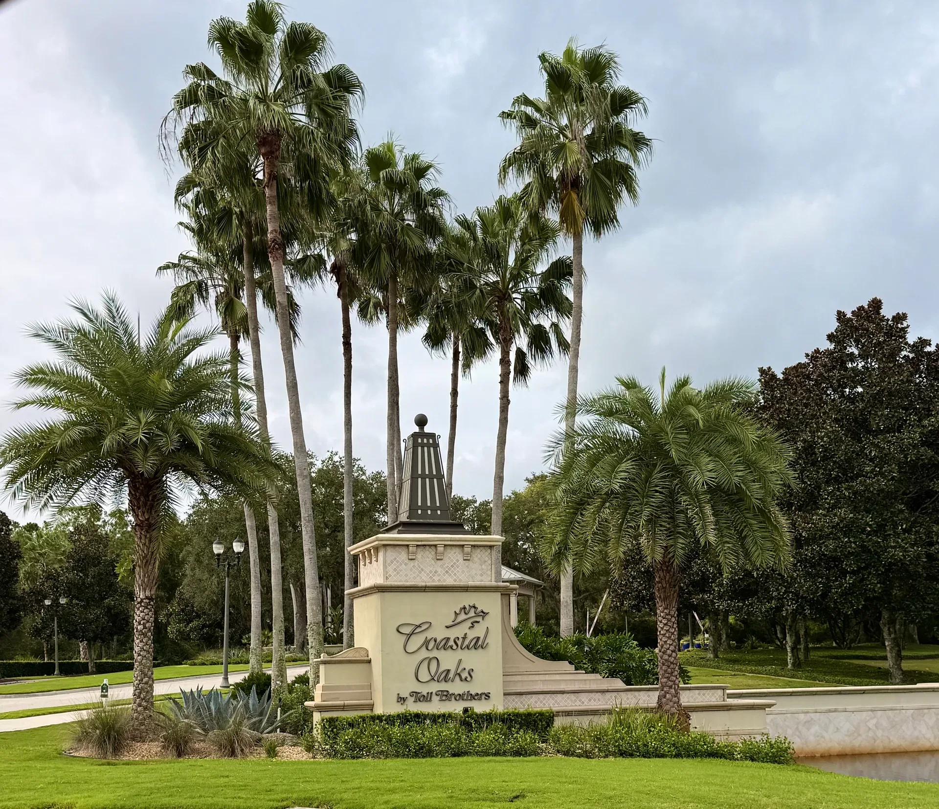 Coastal Oaks entrance monument sign with tall palms and manicured lawns inside the gated community
