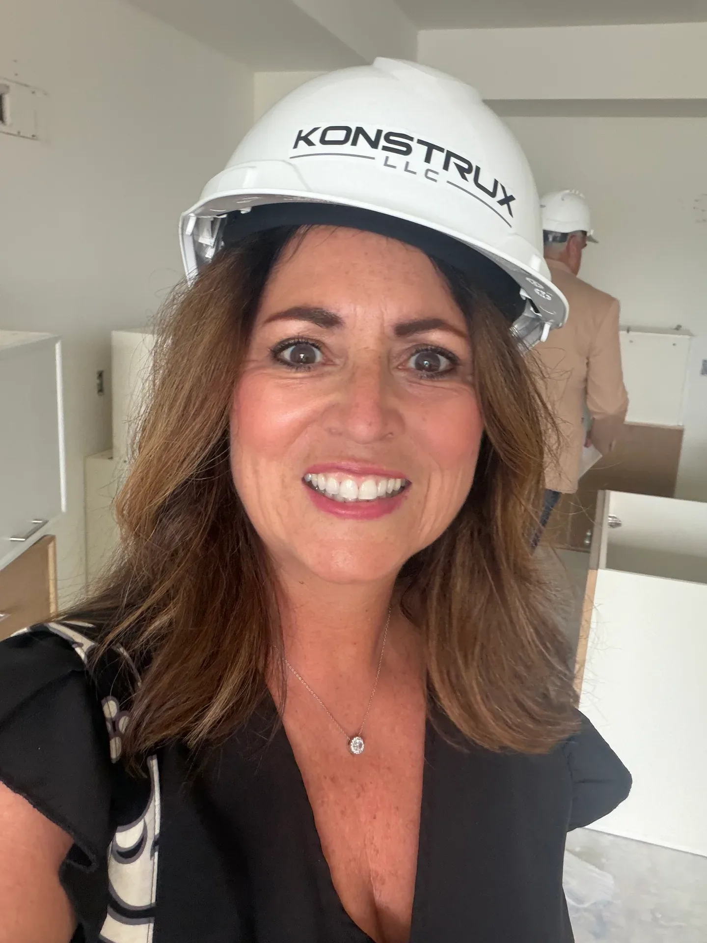 Woman in a white KONSTRUX hard hat smiling at a new construction site with cabinets being installed