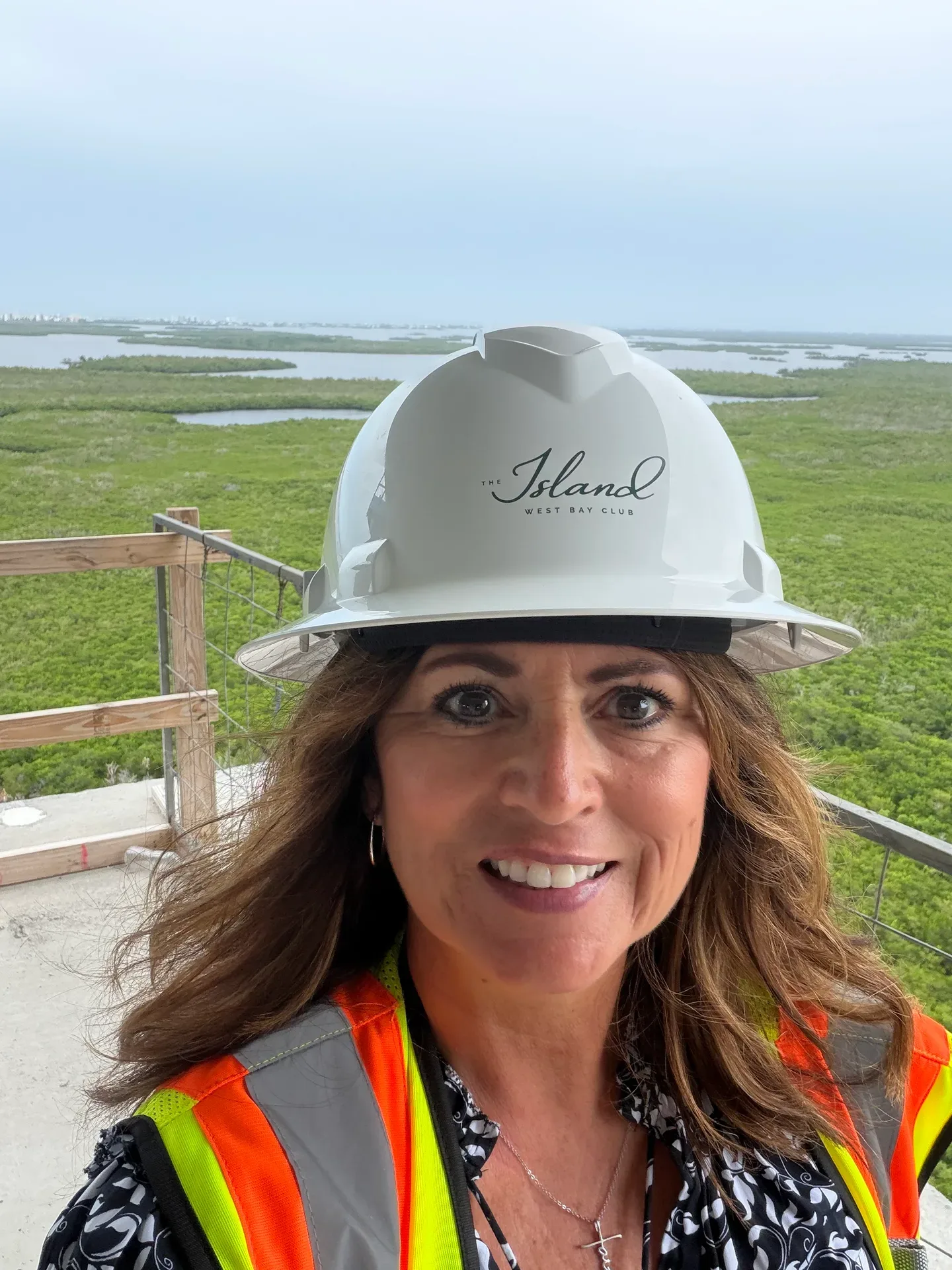 Site selfie in an orange safety vest and hard hat with a coastal marsh backdrop