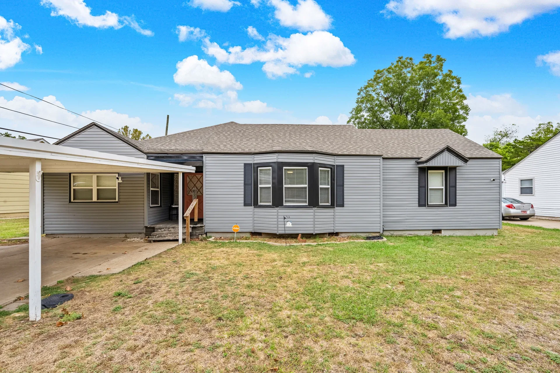 Front exterior of 1211 NW Parkview Blvd, a single-story gray ranch home with a bright coral front door and clear blue sky