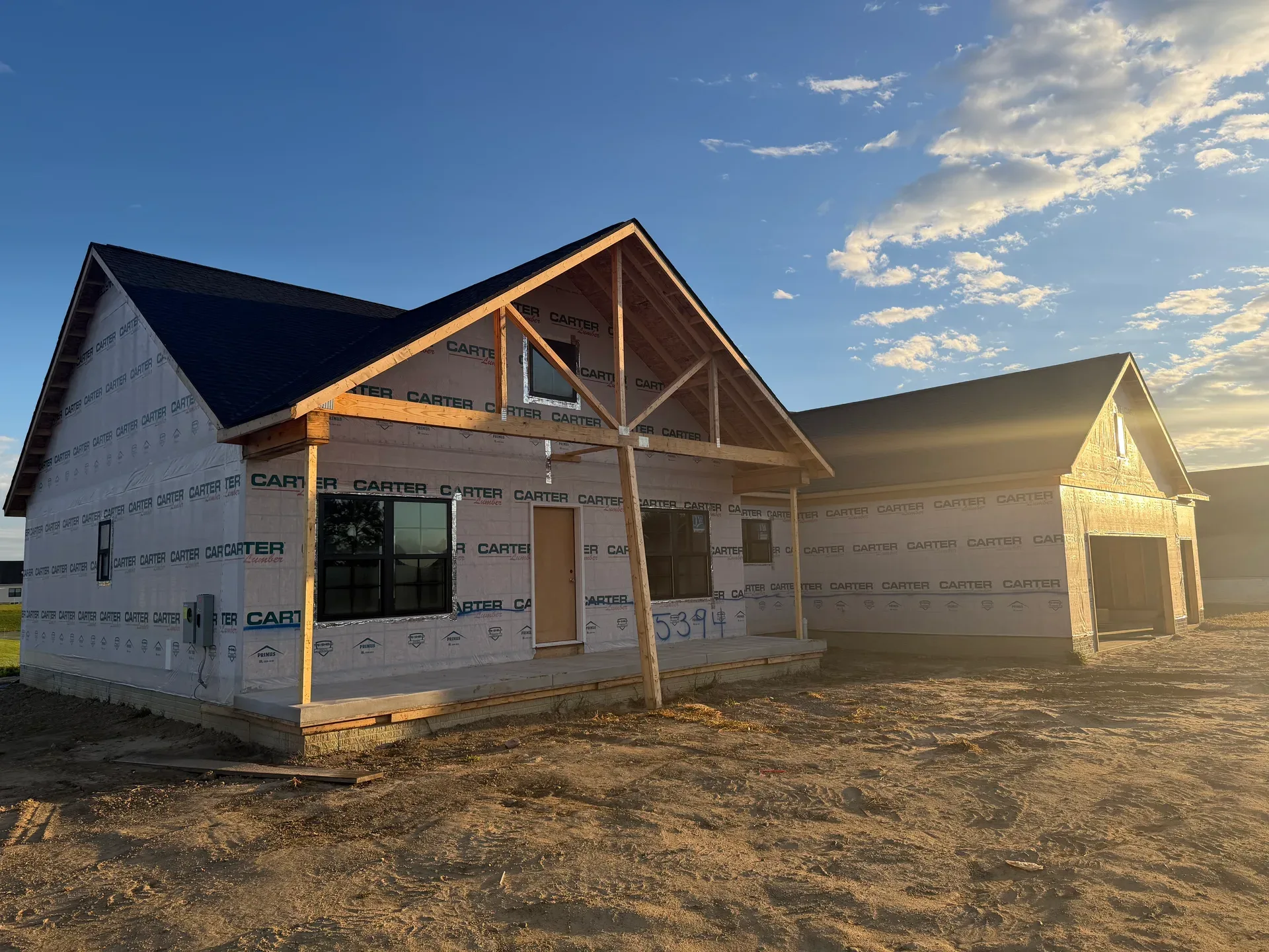 Spec home under construction with timber-framed covered porch at golden hour