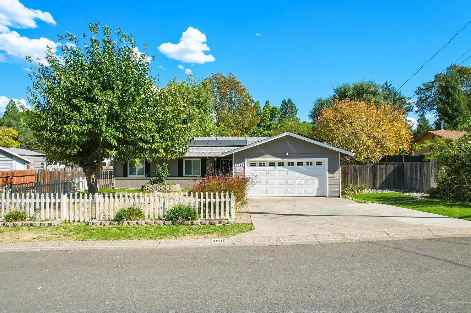 Exterior of 4589 Volo Mine Dr, a single-story ranch home with grey siding, a white picket fence, and a two-car garage in Diamond Springs, California