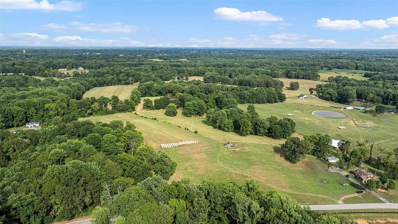 Aerial view of the rolling, partially wooded parcel with a small pond in the distance